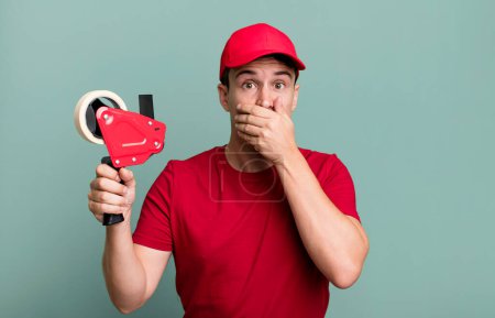 Foto de Adult man covering mouth with hands with a shocked. deliveryman packer concept - Imagen libre de derechos