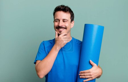 Téléchargez les photos : Homme adulte souriant avec une expression heureuse et confiante avec la main sur le menton. concept de fitness et yoga - en image libre de droit