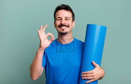 Téléchargez les photos : Homme adulte se sentant heureux, montrant l'approbation avec le geste correct. concept de fitness et yoga - en image libre de droit