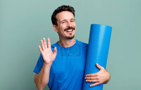 Foto de Hombre adulto sonriendo felizmente, saludándote con la mano, dándote la bienvenida y saludándote. concepto de fitness y yoga - Imagen libre de derechos