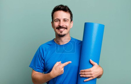 Photo for Adult man smiling cheerfully, feeling happy and pointing to the side. fitness and yoga concept - Royalty Free Image