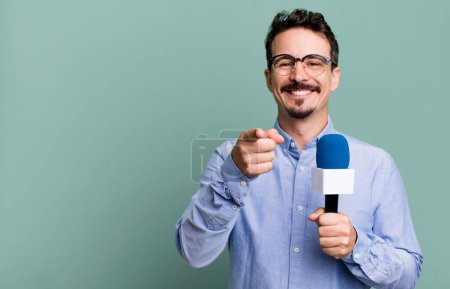 Foto de Adult man pointing at camera choosing you with a microphone. presenter or journalist concept - Imagen libre de derechos