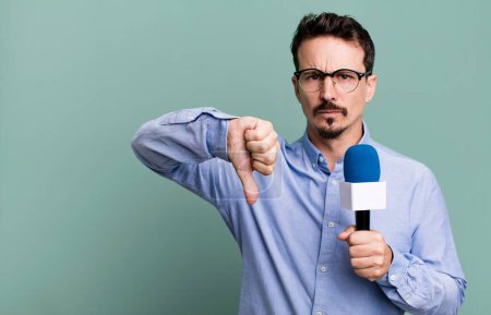 Téléchargez les photos : Adult man feeling cross,showing thumbs down with a microphone. presenter or journalist concept - en image libre de droit