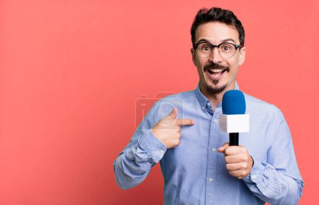 Téléchargez les photos : Adult man feeling happy and pointing to self with an excited with a microphone. presenter or journalist concept - en image libre de droit