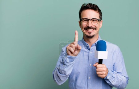 Téléchargez les photos : Adult man smiling proudly and confidently making number one with a microphone. presenter or journalist concept - en image libre de droit