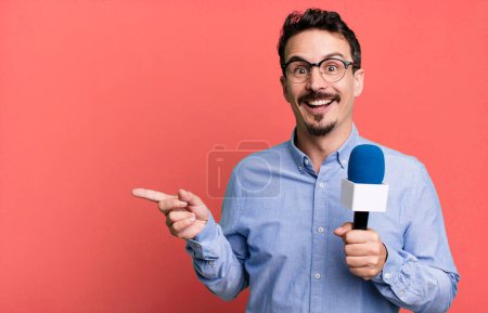 Téléchargez les photos : Adult man smiling cheerfully, feeling happy and pointing to the side with a microphone. presenter or journalist concept - en image libre de droit
