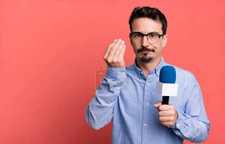 Foto de Adult man making capice or money gesture, telling you to pay with a microphone. presenter or journalist concept - Imagen libre de derechos