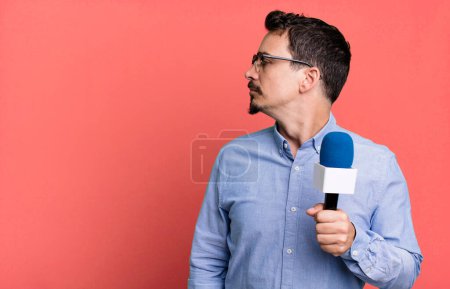 Photo for Adult man on profile view thinking, imagining or daydreaming with a microphone. presenter or journalist concept - Royalty Free Image