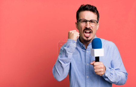 Téléchargez les photos : Adult man shouting aggressively with an angry expression with a microphone. presenter or journalist concept - en image libre de droit