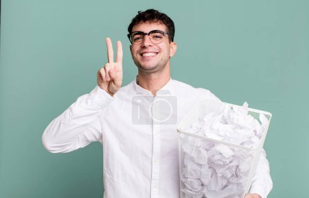 Téléchargez les photos : Homme adulte souriant et regardant heureux, geste de victoire ou de paix. boules de papier erreurs poubelle - en image libre de droit