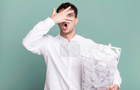 Photo for Adult man looking shocked, scared or terrified, covering face with hand. paper balls mistakes trash - Royalty Free Image
