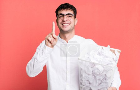 Téléchargez les photos : Homme adulte souriant fièrement et en toute confiance faisant numéro un. boules de papier erreurs poubelle - en image libre de droit