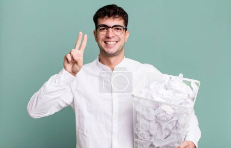 Téléchargez les photos : Homme adulte souriant et regardant amical, montrant numéro deux. boules de papier erreurs poubelle - en image libre de droit