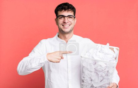 Téléchargez les photos : Homme adulte souriant joyeusement, se sentant heureux et pointant vers le côté. boules de papier erreurs poubelle - en image libre de droit