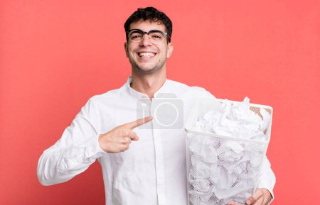 Téléchargez les photos : Homme adulte regardant excité et surpris pointant vers le côté. boules de papier erreurs poubelle - en image libre de droit
