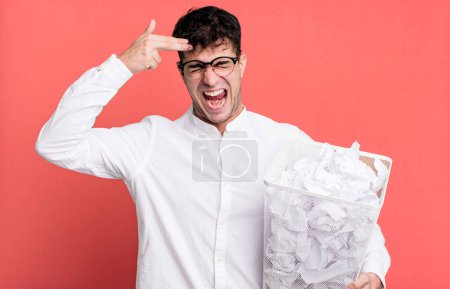 Photo for Adult man looking unhappy and stressed, suicide gesture making gun sign. paper balls mistakes trash - Royalty Free Image
