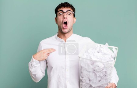 Foto de Hombre adulto mirando sorprendido y sorprendido con la boca abierta, apuntando a sí mismo. bolas de papel errores basura - Imagen libre de derechos