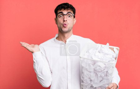 Téléchargez les photos : Homme adulte regardant surpris et choqué, avec la mâchoire tombée tenant un objet. boules de papier erreurs poubelle - en image libre de droit