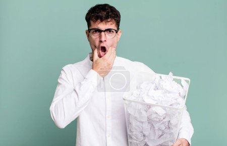 Foto de Hombre adulto con la boca y los ojos bien abiertos y la mano en la barbilla. bolas de papel errores basura - Imagen libre de derechos