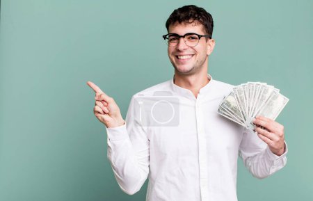 Foto de Hombre adulto sonriendo alegremente, sintiéndose feliz y señalando hacia un lado. concepto de billetes en dólares - Imagen libre de derechos