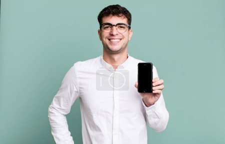 Photo for Adult man smiling happily with a hand on hip and confident and showing his smartphone screen - Royalty Free Image