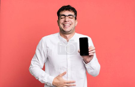 Foto de Hombre adulto riendo en voz alta en algún chiste hilarante y mostrando la pantalla de su teléfono inteligente - Imagen libre de derechos