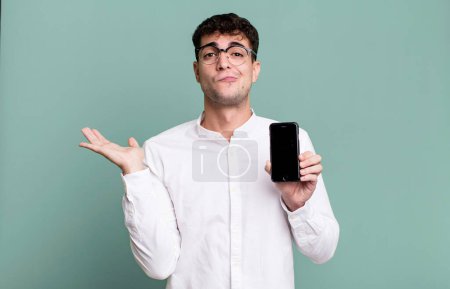 Foto de Hombre adulto se siente desconcertado y confundido y dudando y mostrando la pantalla de su teléfono inteligente - Imagen libre de derechos