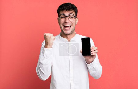 Foto de Hombre adulto se siente sorprendido, riendo y celebrando el éxito y mostrando la pantalla de su teléfono inteligente - Imagen libre de derechos