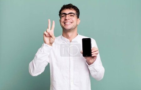 Foto de Hombre adulto sonriendo y mirando feliz, haciendo gestos de victoria o paz y mostrando la pantalla de su teléfono inteligente - Imagen libre de derechos
