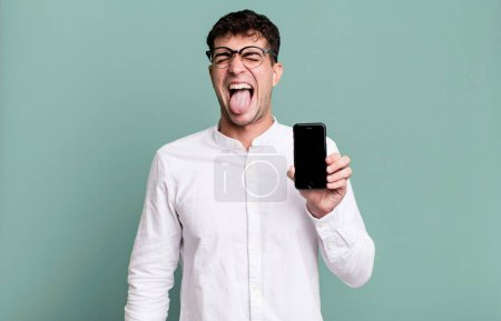 Téléchargez les photos : Homme adulte avec une attitude joyeuse et rebelle, plaisanter et coller la langue et montrer son écran de smartphone - en image libre de droit