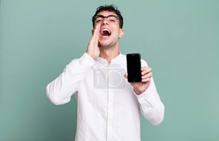 Foto de Hombre adulto sentirse feliz, dando un gran grito con las manos al lado de la boca y mostrando la pantalla de su teléfono inteligente - Imagen libre de derechos