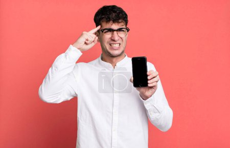 Téléchargez les photos : Homme adulte se sentant confus et perplexe, montrant que vous êtes fou et montrant son écran de smartphone - en image libre de droit