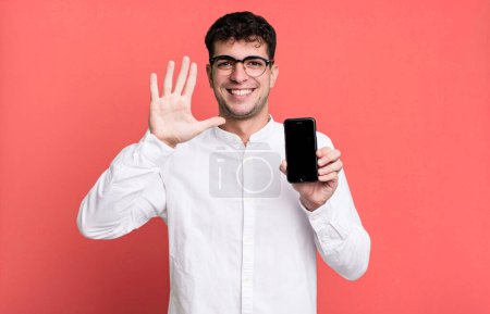 Téléchargez les photos : Homme adulte souriant et regardant amical, montrant le numéro cinq et montrant son écran de smartphone - en image libre de droit