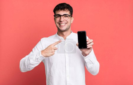 Téléchargez les photos : Homme adulte regardant excité et surpris pointant vers le côté et montrant son écran de smartphone - en image libre de droit