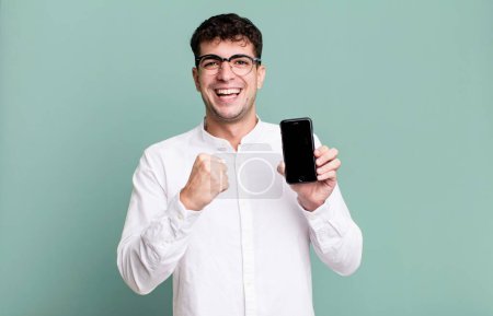 Téléchargez les photos : Homme adulte se sentir heureux et faire face à un défi ou célébrer et montrer son écran de smartphone - en image libre de droit