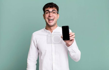 Téléchargez les photos : Homme adulte regardant heureux et agréablement surpris et montrant son écran de smartphone - en image libre de droit