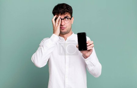 Téléchargez les photos : Homme adulte se sentant ennuyé, frustré et somnolent après un fatigant et montrant son écran de smartphone - en image libre de droit