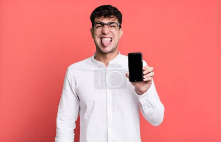 Foto de Hombre adulto sentirse disgustado e irritado y la lengua hacia fuera y mostrando la pantalla de su teléfono inteligente - Imagen libre de derechos