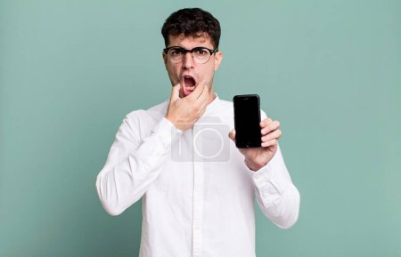 Photo for Adult man with mouth and eyes wide open and hand on chin and showing his smartphone screen - Royalty Free Image