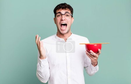 Téléchargez les photos : Homme adulte se sentant heureux et étonné de quelque chose d'incroyable tenant un bol de nouilles ramen - en image libre de droit