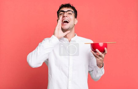 Téléchargez les photos : Homme adulte se sentant heureux, donnant un grand cri avec les mains à côté de la bouche tenant un bol de nouilles ramen - en image libre de droit