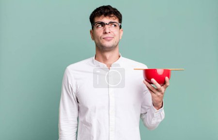 Téléchargez les photos : Homme adulte haussant les épaules, se sentant confus et incertain tenant un bol de nouilles ramen - en image libre de droit