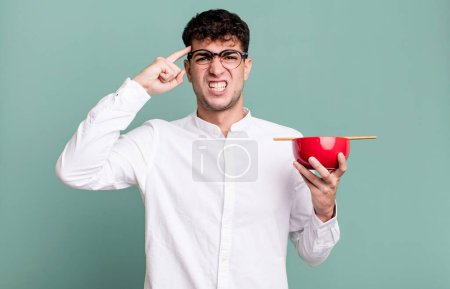 Téléchargez les photos : Homme adulte se sentant confus et perplexe, montrant que vous êtes fou tenant un bol de nouilles ramen - en image libre de droit