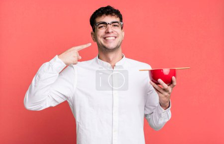 Photo for Adult man smiling confidently pointing to own broad smile holding a ramen noodles bowl - Royalty Free Image
