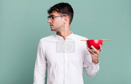 Photo for Adult man on profile view thinking, imagining or daydreaming holding a ramen noodles bowl - Royalty Free Image