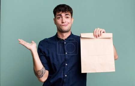 Photo for Adult man feeling puzzled and confused and doubting with a take away breakfast paper bag with a take away breakfast paper bag - Royalty Free Image