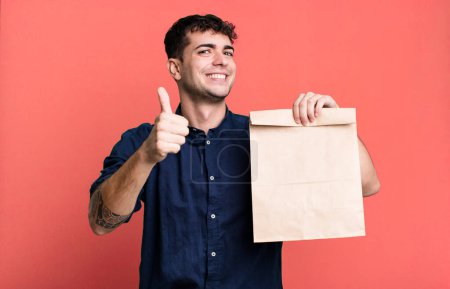 Photo for Adult man feeling proud,smiling positively with thumbs up with a take away breakfast paper bag with a take away breakfast paper bag - Royalty Free Image