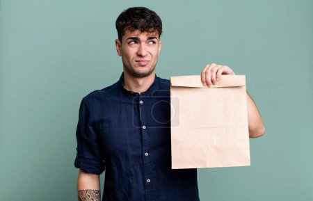 Téléchargez les photos : Homme adulte se sentant triste, bouleversé ou en colère et regardant vers le côté avec un sac en papier de petit déjeuner à emporter avec un sac en papier de petit déjeuner à emporter - en image libre de droit