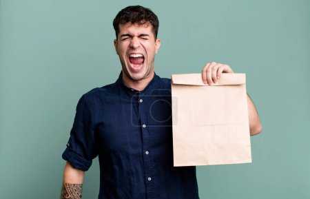 Téléchargez les photos : Homme adulte criant agressivement, regardant très en colère avec un sac de papier de petit déjeuner à emporter avec un sac de papier de petit déjeuner à emporter - en image libre de droit