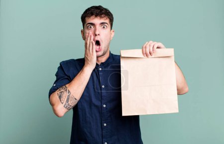 Téléchargez les photos : Homme adulte se sentant choqué et effrayé avec un sac en papier à emporter petit déjeuner avec un sac en papier à emporter petit déjeuner - en image libre de droit